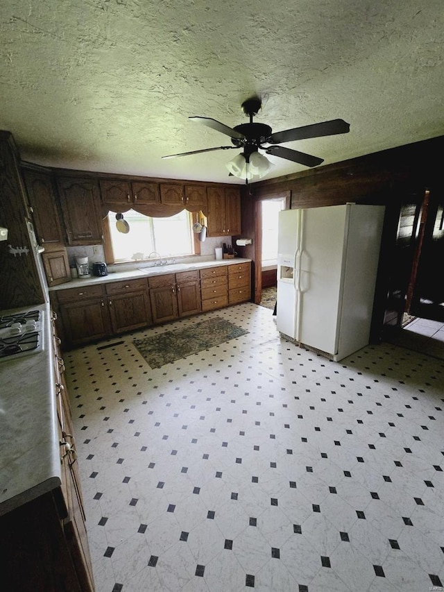 kitchen featuring a textured ceiling, white fridge with ice dispenser, ceiling fan, and light tile floors