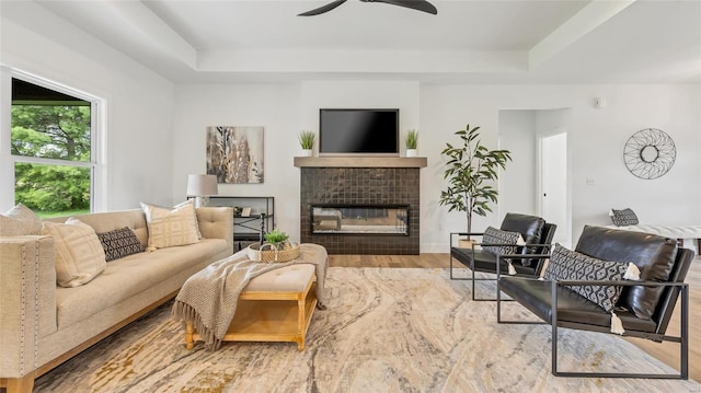 living room with hardwood / wood-style flooring, a raised ceiling, and a tiled fireplace