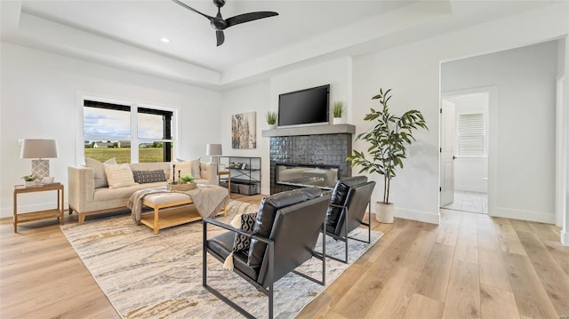 living room with a tray ceiling, ceiling fan, light hardwood / wood-style flooring, and a brick fireplace