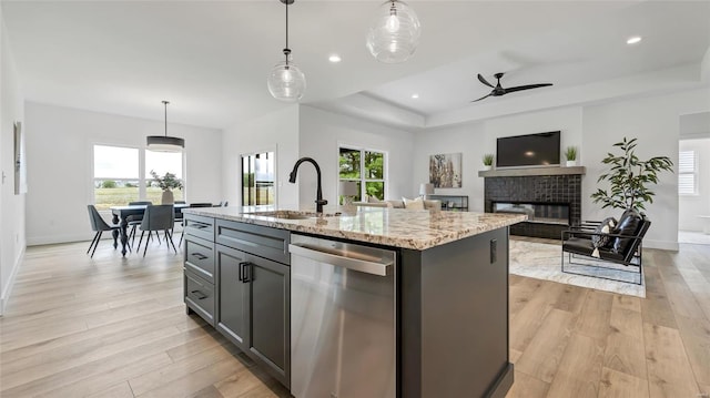 kitchen featuring stainless steel dishwasher, ceiling fan, a center island with sink, a fireplace, and hanging light fixtures