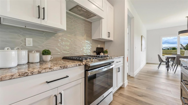 kitchen featuring exhaust hood, stainless steel gas range, tasteful backsplash, light stone counters, and white cabinetry