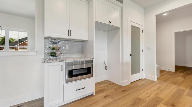 bar featuring light stone countertops, white cabinetry, backsplash, and light hardwood / wood-style flooring