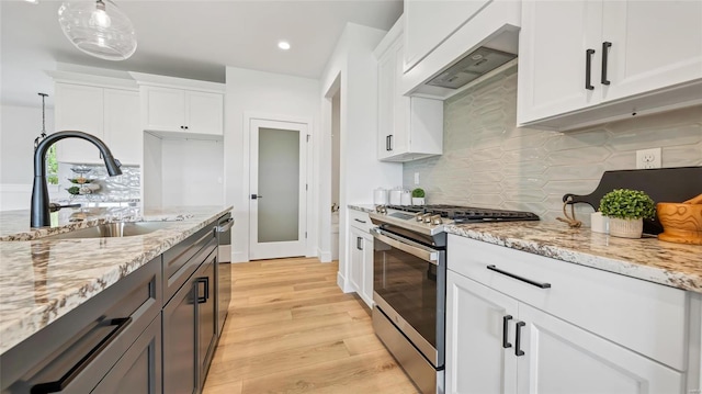 kitchen with appliances with stainless steel finishes, light stone counters, sink, pendant lighting, and white cabinetry