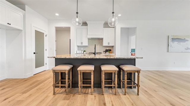 kitchen with white cabinetry, an island with sink, light stone countertops, and decorative light fixtures