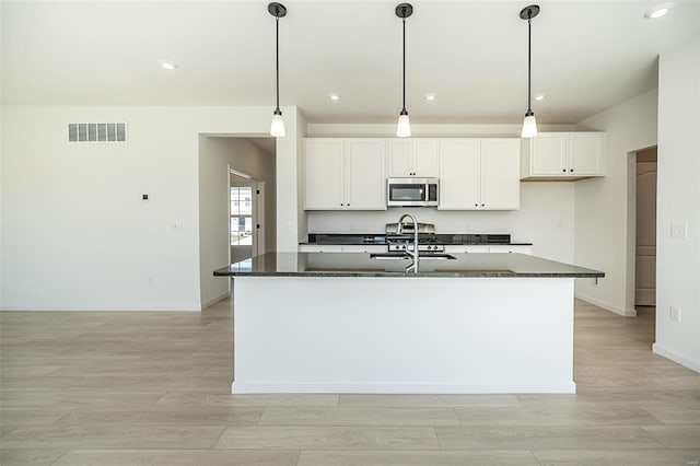 kitchen with pendant lighting, a kitchen island with sink, dark stone counters, white cabinetry, and stainless steel appliances