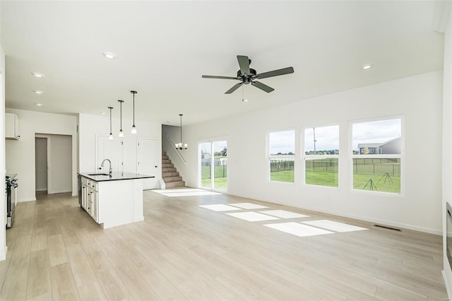 unfurnished living room featuring sink, light hardwood / wood-style floors, and ceiling fan with notable chandelier