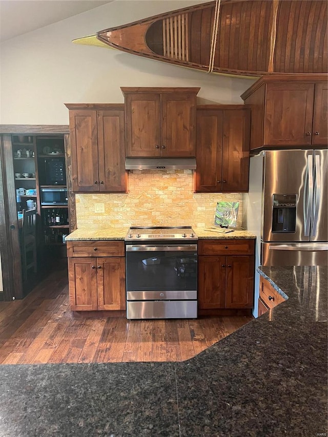 kitchen with tasteful backsplash, dark stone counters, dark wood-type flooring, and stainless steel appliances