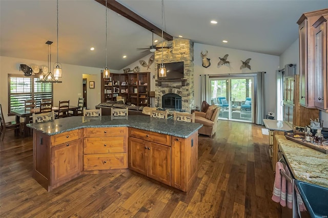 kitchen with beamed ceiling, ceiling fan, a stone fireplace, and dark hardwood / wood-style floors