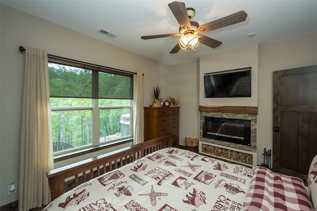 bedroom with a stone fireplace, multiple windows, and ceiling fan