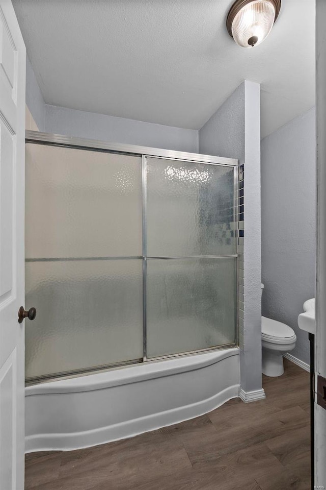 bathroom featuring hardwood / wood-style flooring, toilet, and bath / shower combo with glass door