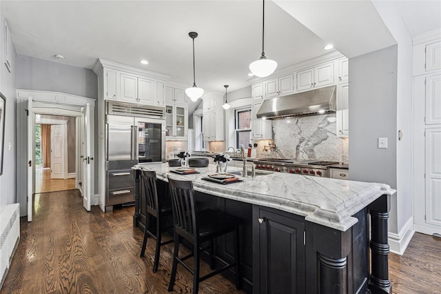 kitchen featuring backsplash, sink, an island with sink, white cabinets, and built in fridge