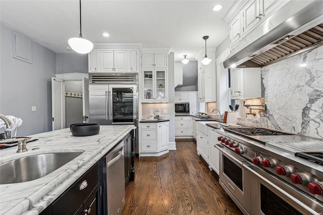 kitchen featuring pendant lighting, white cabinets, built in appliances, sink, and light stone counters