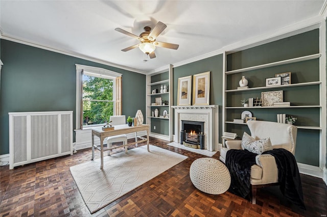 home office featuring radiator heating unit, ceiling fan, dark parquet floors, crown molding, and built in shelves