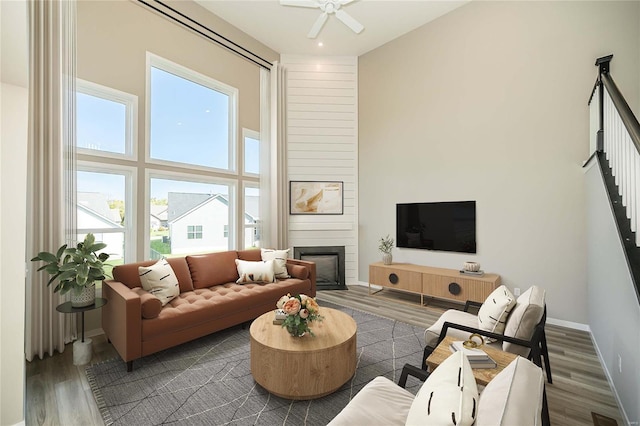 living room featuring a large fireplace, ceiling fan, hardwood / wood-style floors, and a high ceiling