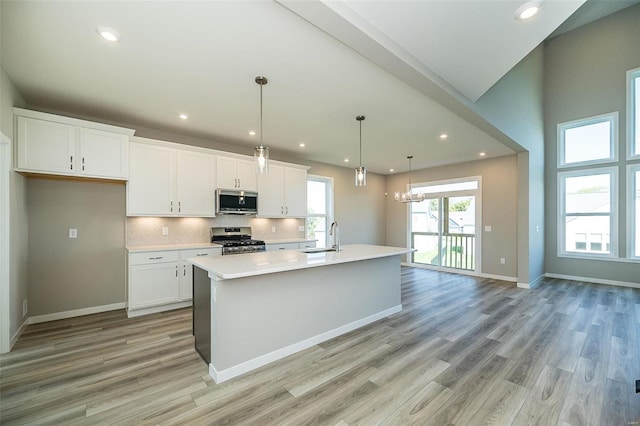 kitchen featuring white cabinetry, hanging light fixtures, stainless steel appliances, a kitchen island with sink, and light wood-type flooring