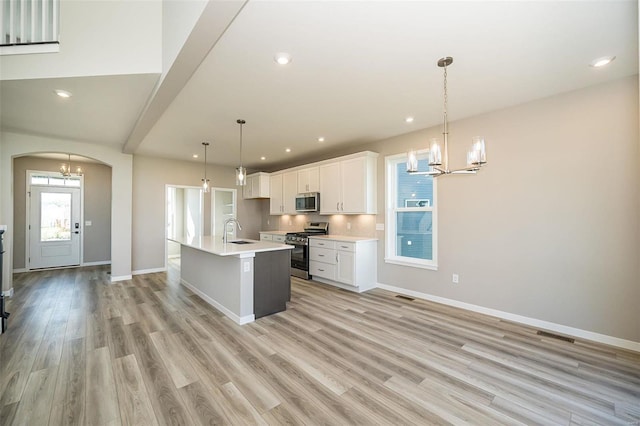 kitchen featuring stainless steel appliances, pendant lighting, light hardwood / wood-style floors, white cabinetry, and an island with sink