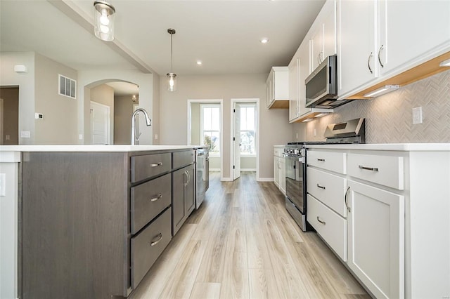 kitchen with stainless steel appliances, decorative light fixtures, a center island with sink, light hardwood / wood-style flooring, and white cabinetry