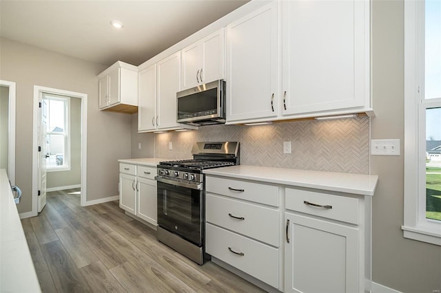 kitchen featuring decorative backsplash, stainless steel appliances, white cabinetry, and light hardwood / wood-style flooring