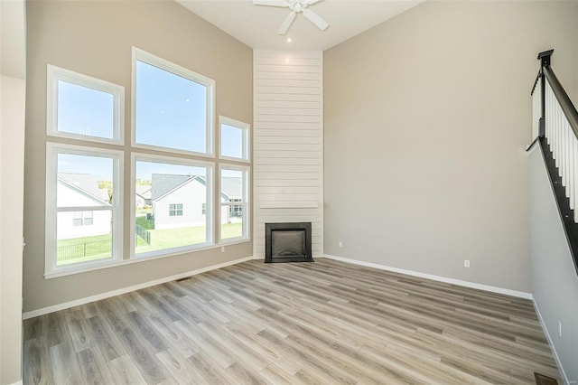 unfurnished living room featuring a large fireplace, ceiling fan, light hardwood / wood-style floors, and a high ceiling