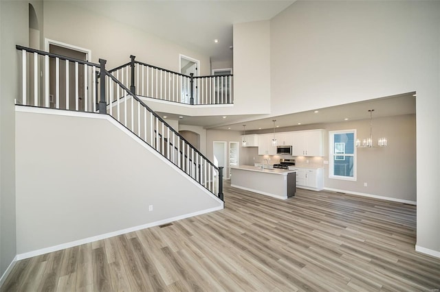 unfurnished living room featuring a notable chandelier, a towering ceiling, sink, and light hardwood / wood-style flooring