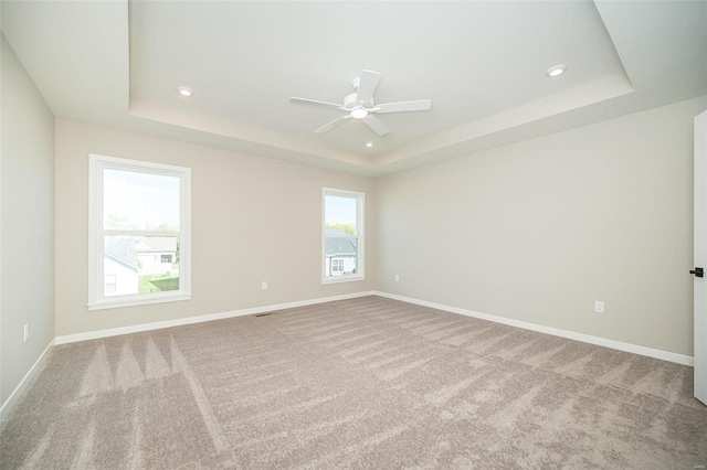 spare room with a raised ceiling, light carpet, and ceiling fan