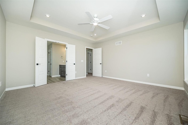 unfurnished bedroom featuring carpet, ceiling fan, a raised ceiling, and ensuite bathroom