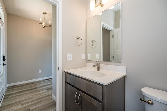 bathroom with wood-type flooring, vanity, toilet, and a notable chandelier