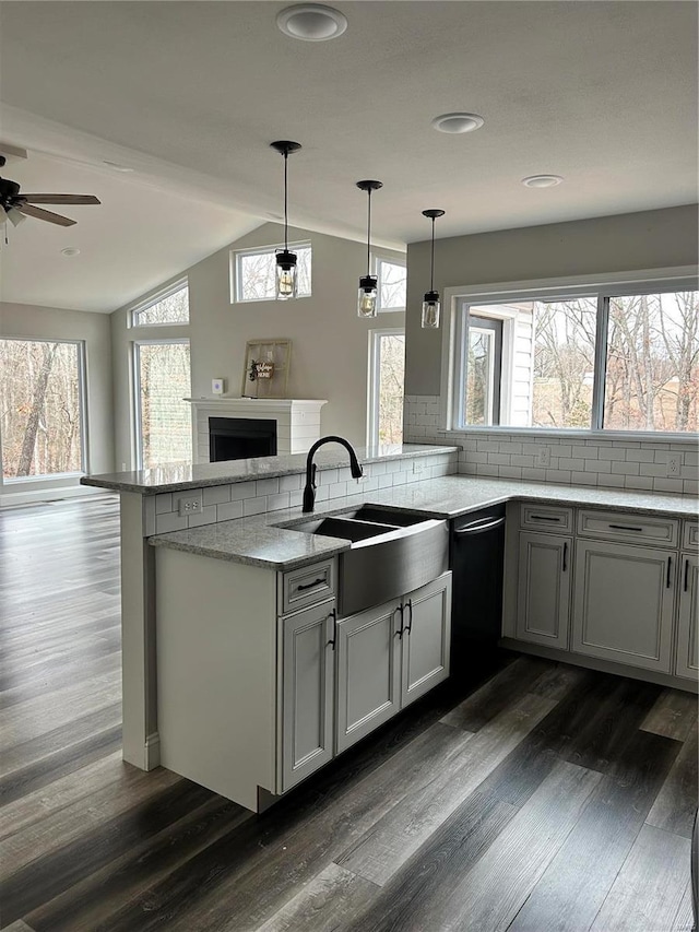 kitchen featuring dark wood-type flooring, sink, hanging light fixtures, kitchen peninsula, and light stone countertops