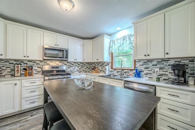 kitchen with sink, light hardwood / wood-style flooring, decorative backsplash, appliances with stainless steel finishes, and white cabinetry