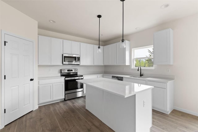 kitchen featuring wood-type flooring, white cabinets, stainless steel appliances, sink, and a kitchen island