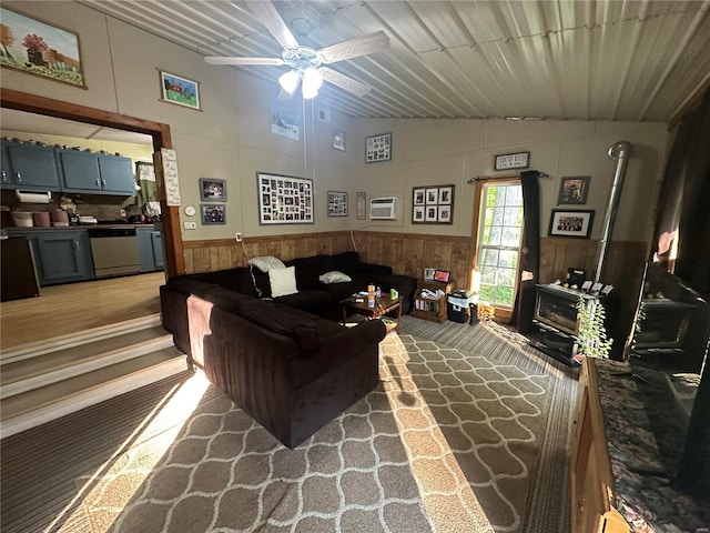 living room featuring a wall unit AC, a wood stove, ceiling fan, and lofted ceiling