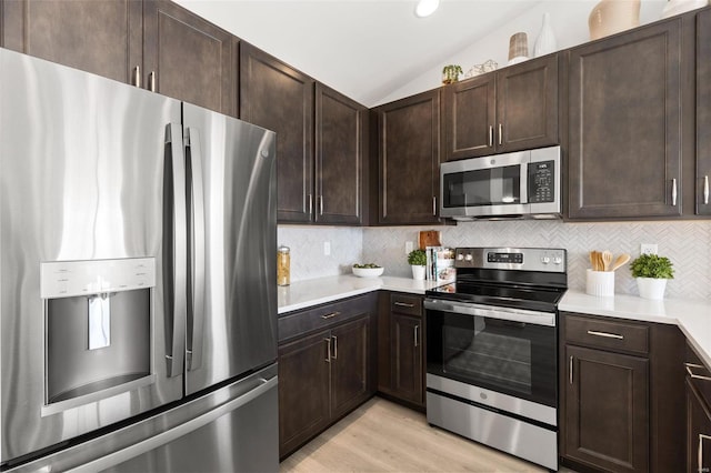 kitchen featuring backsplash, appliances with stainless steel finishes, vaulted ceiling, light hardwood / wood-style floors, and dark brown cabinetry