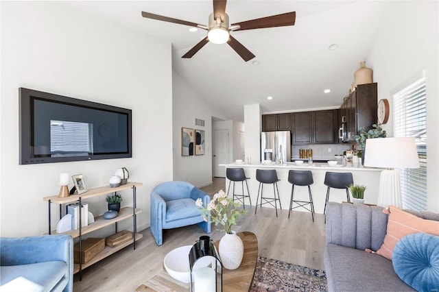 living room with high vaulted ceiling, ceiling fan, and light wood-type flooring