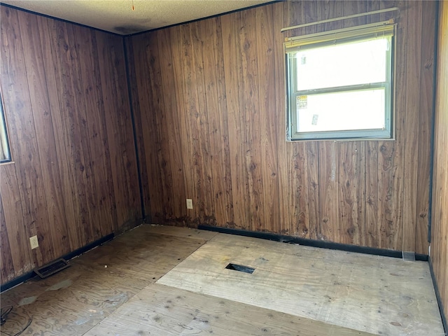 unfurnished room featuring a textured ceiling and wooden walls