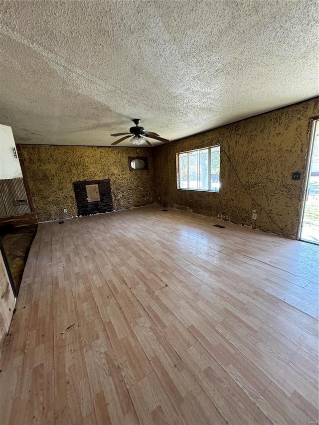 unfurnished living room with a large fireplace, wood-type flooring, ceiling fan, and a textured ceiling