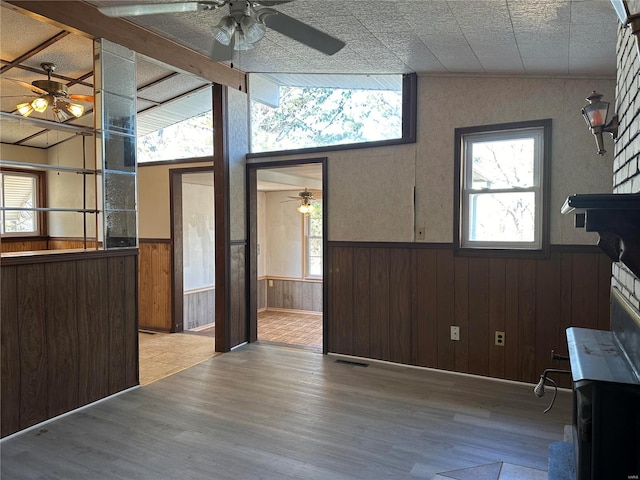 unfurnished living room with vaulted ceiling, wooden walls, hardwood / wood-style flooring, and ceiling fan