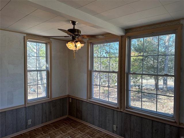 unfurnished room featuring beamed ceiling, a wealth of natural light, ceiling fan, and parquet flooring