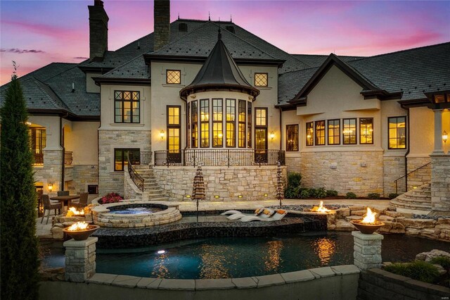 back house at dusk featuring a pool with hot tub and an outdoor fire pit