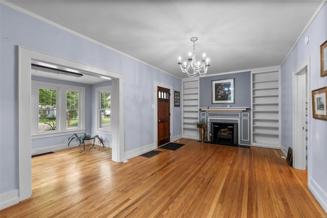 unfurnished living room with built in shelves, a chandelier, light wood-type flooring, and ornamental molding