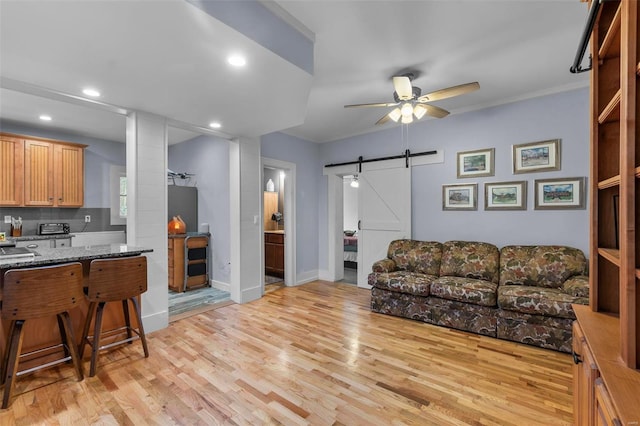 living room with a barn door, light wood-type flooring, and ceiling fan