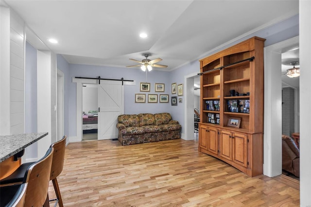 living room featuring a barn door, ceiling fan, and light hardwood / wood-style floors