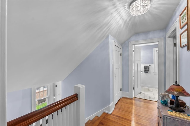 hallway with a notable chandelier, vaulted ceiling, and light hardwood / wood-style flooring