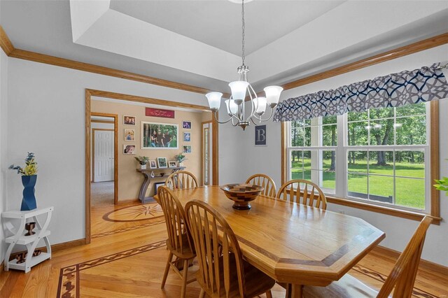 dining area with light wood-type flooring, a tray ceiling, and a chandelier