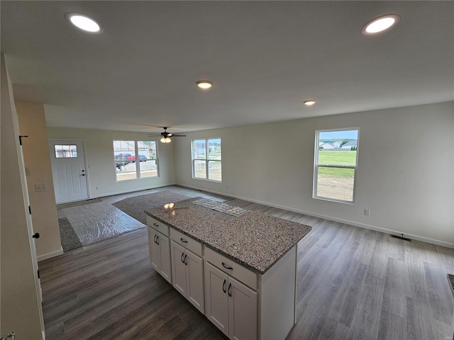 kitchen with a center island, dark hardwood / wood-style flooring, light stone countertops, and white cabinets