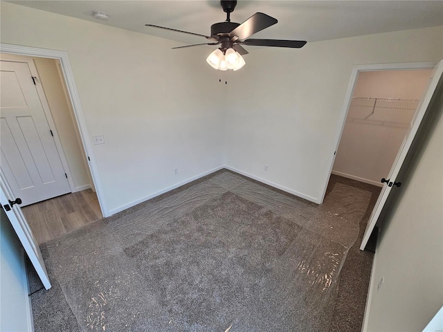 unfurnished bedroom featuring dark colored carpet, ceiling fan, a walk in closet, and a closet