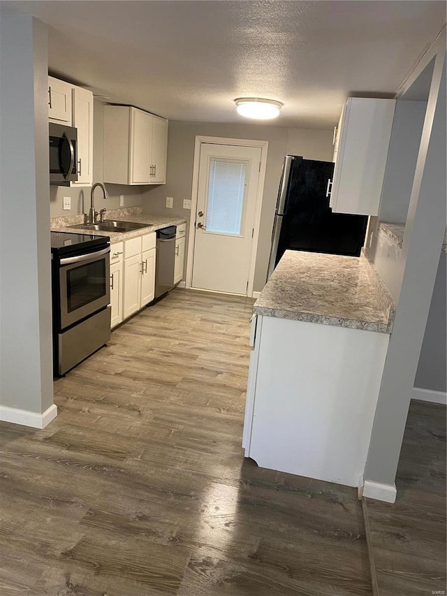 kitchen with light hardwood / wood-style floors, white cabinets, appliances with stainless steel finishes, and sink