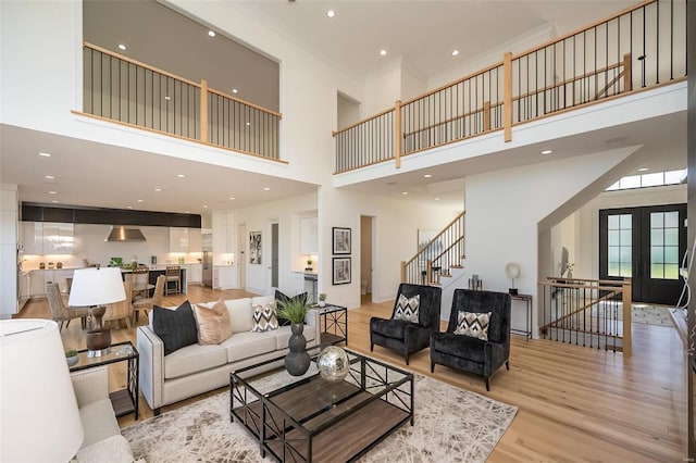 living room with light hardwood / wood-style floors, french doors, ornamental molding, and a towering ceiling