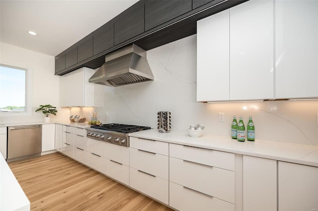 kitchen featuring stainless steel appliances, wall chimney range hood, white cabinetry, and light wood-type flooring