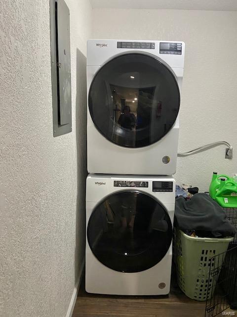 laundry room with stacked washer and dryer, electric panel, a textured wall, and wood finished floors