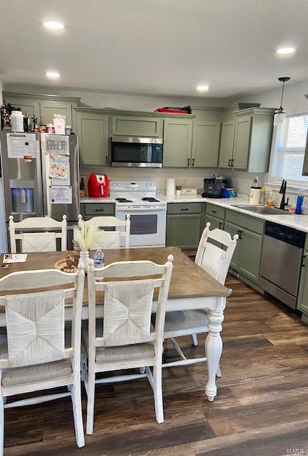 kitchen featuring stainless steel appliances, dark wood-type flooring, a sink, light countertops, and green cabinetry